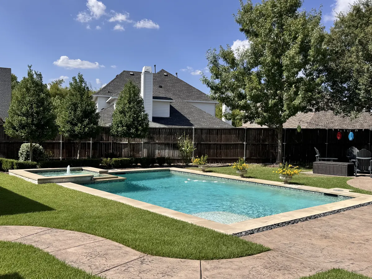 Sparkling clean backyard pool with a raised spa spillover, green lawn and fenced yard in North Texas